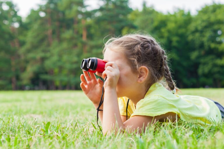 little girl looking through binoculars on summer day